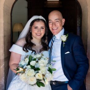 Bride with her father beautifully lit in the main doorway entrance at the hotel as they leave for the nearby church