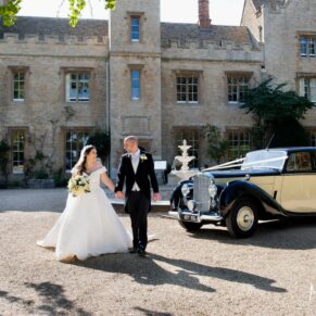 The newlyweds walk beside their stunning vintage wedding car in front of Weston Manor Hotel