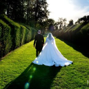 The newlyweds walking into the sun along a sweeping topiary avenue in Weston Manor's stunning gardens