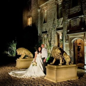 Floodlit pose of the newlyweds between the stone lions at the entrance to Weston Manor
