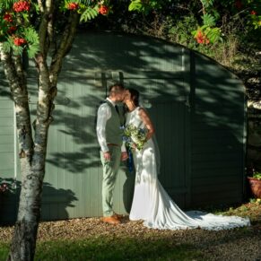 The newlyweds captured in the dappled light next to a rustic barn surrounded by red berries