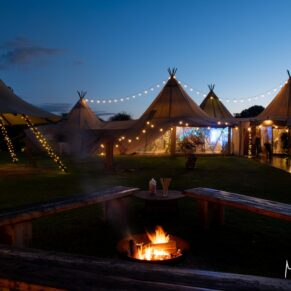 Night-time view across the firepit outside the illuminated tipi