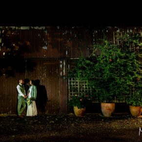 The newlyweds pose for the camera at night-time outside the atmospheric floodlit barn at their Dovecote Events wedding