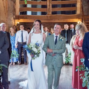 The bride makes her grand entrance into the barn on her father's arm