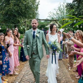 The smiling newlyweds dash through the confetti aisle in the paddock gardens