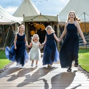 The flower girls captured running towards the camera with the tipi in the background