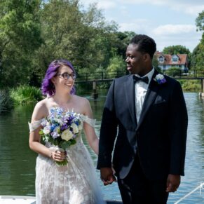 The newlyweds take a stroll beside the River Thames on this glorious sunny day at their Great House wedding in Sonning