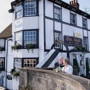 The bride and groom in the town centre before their wedding reception looking across the Thames with a pub as the backdrop
