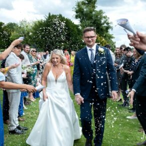 The smiling bride and groom dash through the colourful confetti aisle at their Latimer Estate wedding