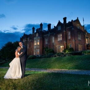 The Latimer Estate dramatically floodlit at night-time with the smiling newlyweds in the foreground
