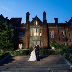 The Latimer Estate floodlit photography at night-time with the newlyweds in the foreground on the steps of the wedding venue