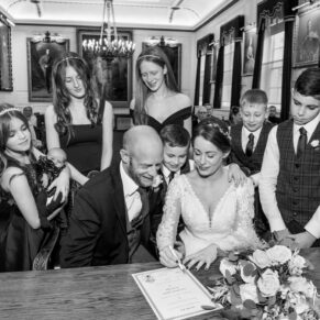 The smiling newlyweds sign the marriage register with their witnesses watching over at their Windsor Guildhall wedding