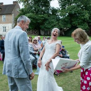 Photography of a giggling bride who didn't seem to mind when the celebrant dropped the rings during her Bisham Abbey wedding ceremony