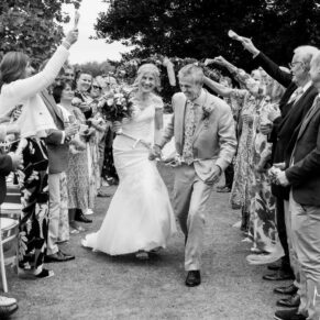 Photography of the happy newlyweds dashing through the confetti aisle after their Bisham Abbey civil wedding ceremony in the venue's gardens