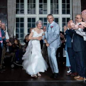 Photography of these Bisham Abbey newlyweds dashing through the human aisle at their evening wedding reception during the Ceilidh
