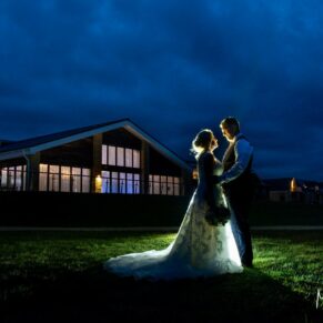 The newlyweds pose for a dramatic photo outside the Cotswolds Hotel, Golf and Spa at dusk on their wedding day