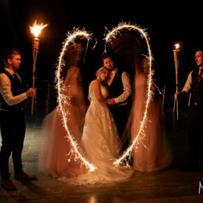 Photography of the bridal party creating a sparkler heart around the newlyweds after nightfall at their Cotswolds Hotel, Golf and Spa evening wedding reception