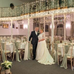 A wide view of a Christmassy wedding breakfast setup inside the Kings Chapel in Old Amersham with the newlyweds in the foreground