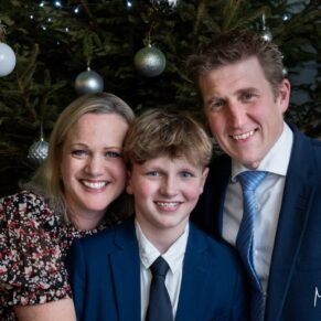 A smiley wedding family portrait in front of the Christmas tree at The Kings Chapel in Old Amersham