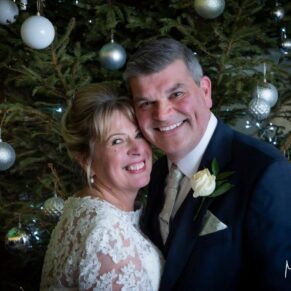The newlyweds pose for a portrait beside the Christmas tree at their Kings Chapel wedding reception in Old Amersham
