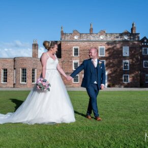 The newlyweds take a stroll in front of Meols Hall on their wedding day under perfect blue skies