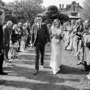 The smiling newlyweds dash through the confetti aisle at their Manor House Hotel wedding reception in Moreton-in-Marsh