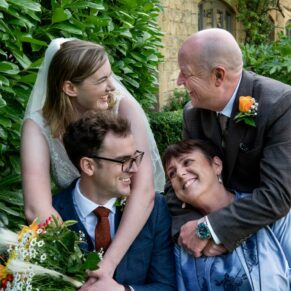 The newlyweds enjoy a hug with the groom's parents at their Manor House Hotel wedding in Moreton-in-Marsh