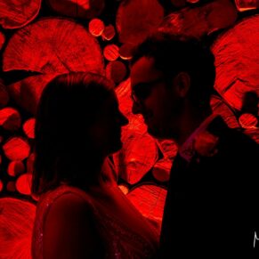 The Manor House Hotel has so many fabulous backdrops for a wedding day, including this striking wood stack. For this pose I've used a coloured uplighter to create the dramatic lighting effect you see here, whilst placing the newlyweds in silhouette in the foreground completes the wow factor. At each and every wedding I attend, my lighting tricks are deployed for these surreal effects. The bride and groom pose beside an illuminated log stack at their Manor House Hotel wedding reception in Moreton-in-Marsh