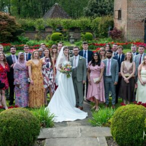 The bride and groom pose for a group photograph in the colourful gardens with some friends during their Chenies Manor drinks reception