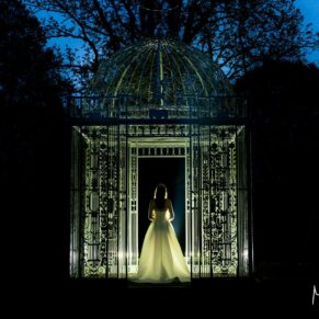Dramatic dusk portrait of the bride under the wrought iron rose arbour at her Chenies Manor spring wedding