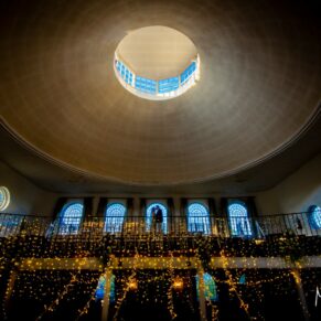 I’m always looking to capture some dramatic & thought-provoking poses on a wedding day! This scene was shot inside the wonderful Kings Chapel wedding venue in Old Amersham. And with an incredible wow backdrop like this, and with masses of sparkling fairy lights added to the mix, it’s almost impossible to go wrong! There's just so much happening in this image, but ultimately our eyes are drawn to the silhouetted kissing couple in the centre. A dramatic wide angle shot of the wedding interiors at The Kings Chapel's in Old Amersham with the silhouetted newlyweds placed in a central window