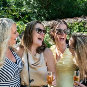 A candid wedding moment between friends filled with laughter in the gardens at The Kings Chapel Old Amersham