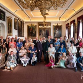 A large group pose of the newlyweds with all of their wedding guests inside the Windsor Guildhall on their wedding day