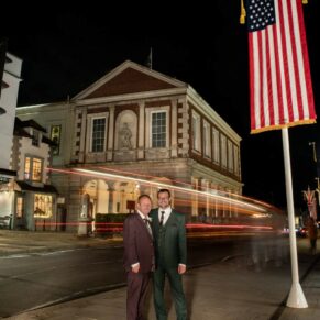 A floodlit pose of the newlyweds with car headlights streaking through the backdrop after nightfall outside the Windsor Guildhall on their wedding day