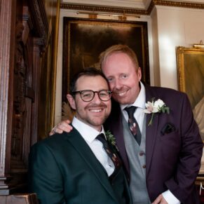 The smiling newlyweds pose for a regal portrait beside portraits of the Kings and Queens of England after their Windsor Guildhall wedding ceremony