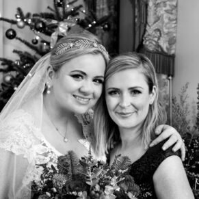 Black and white wedding photography of bride with her bridesmaid next to a Christmas tree at Cliveden House their Buckinghamshire venue