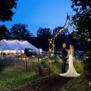 Buckinghamshire wedding photography of the newlyweds in a dramatic floodlit night pose, whilst capturing the illuminated marquee in the distance