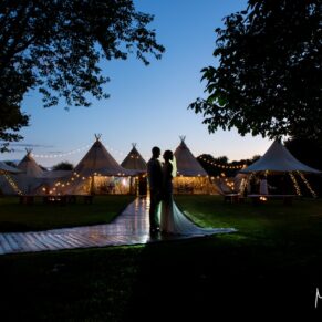 Buckinghamshire marquee wedding photography of the newlyweds at dusk, whilst capturing the festival tipi setup in the background