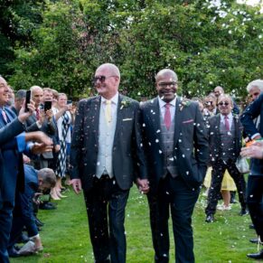 Photography of the happy newlyweds walking through the colourful confetti aisle in the gardens of their Badgemore Park wedding in Henley on Thames