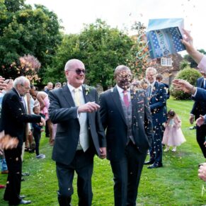 Photography of the smiling newlyweds dashing through the confetti aisle in the gardens at their Badgemore Park summer wedding in Oxfordshire