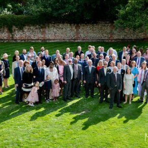 Photography of the newlyweds with all of their guests in the gardens at their Badgemore Park summer wedding in Oxfordshire