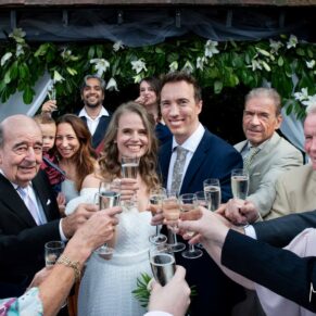 Photography of the bride and groom with their guests charging champagne glasses at the camera in the gardens at their Fredrick's Hotel wedding in Berkshire