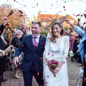 Colourful confetti photography of the happy bride and groom dashing between their wedding guests at their Winters Tale Country Barn venue in Buckinghamshire