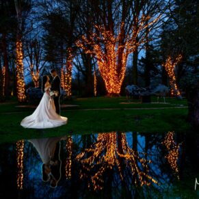 Night-time floodlit wedding photography of the newlyweds with dramatic water reflections at The Crazy Bear Hotel in Stadhampton